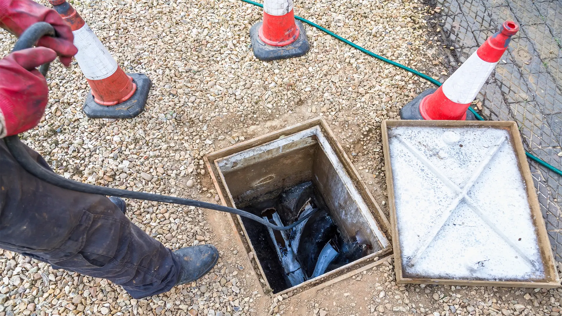 A man is standing in the hole of an open sewer.