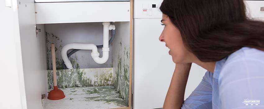 A woman looking at the pipes in her home.