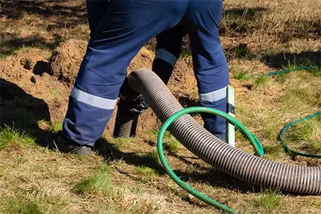 A person in blue pants and green boots is holding a hose.