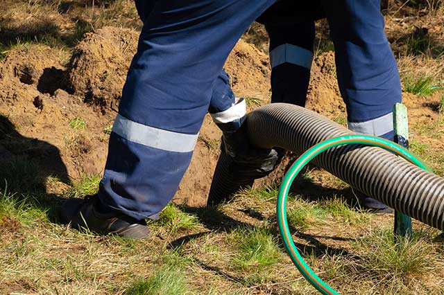 A person with blue pants and green hose is standing next to a pipe.