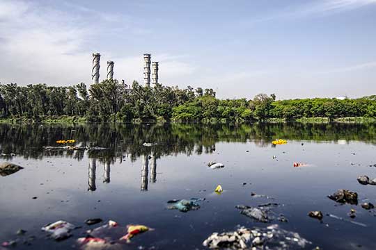 A river contaminated by debris with an industrial factory in the background