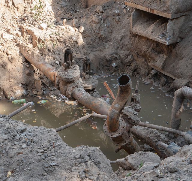 A man is standing in the water near some pipes.