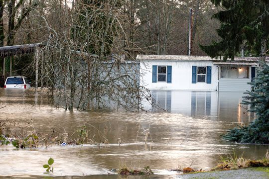 A flooded trailer home with trees in the background.