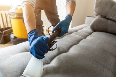 A person in blue gloves is using a cloth to clean the couch.