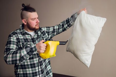 A man holding a pillow while using an electric iron.