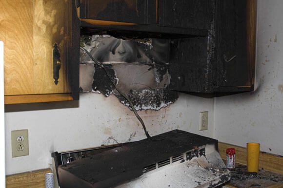 A kitchen with black cabinets and a fire damaged wall.