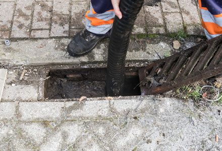 A person standing on the side of a street next to a hole.