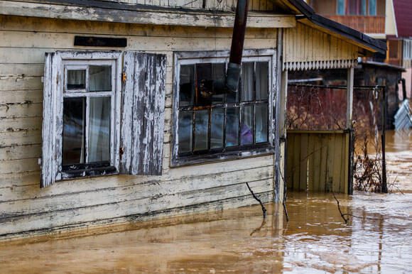 A flooded house with water pouring out of the windows.