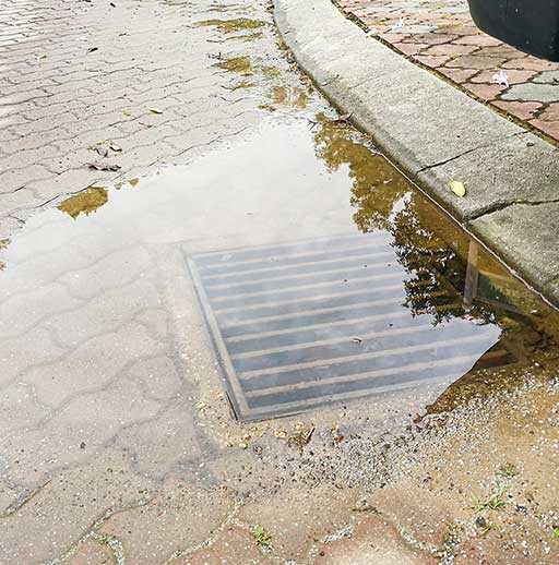 A puddle of water on the ground next to a sidewalk.