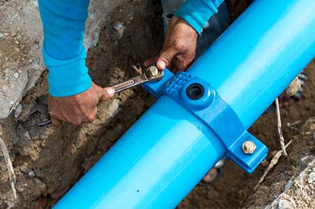 A man using a wrench to tighten a bolt on a blue water pipe